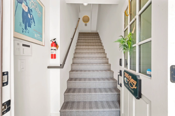 Entry stairway with soft gray carpet runner, white walls, framed artwork, and natural light leading to upper level